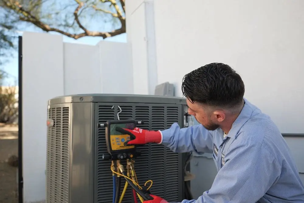 Day & Night Air Conditioning, Heating, and Plumbing technician performing commercial HVAC service in Phoenix Arizona while checking a digital diagnostic gauge connected to an outdoor AC unit. The technician is using hoses and testing equipment to measure system pressure and performance. The scene represents commercial HVAC in Phoenix Arizona including air conditioning repair, system diagnostics, and routine maintenance. Customers can contact Day & Night Air Conditioning, Heating, and Plumbing at (602) 584-7758 for commercial HVAC services including repair, installation, and maintenance.