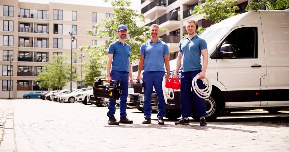 Three Day & Night Air Conditioning, Heating, and Plumbing technicians standing next to a service van in a Phoenix Arizona setting while holding HVAC tools and equipment. The scene represents commercial HVAC in Phoenix Arizona where technicians provide repair, installation, and maintenance services for business and residential properties. The tools include hoses, toolboxes, and service gear used for HVAC system diagnostics and service work. Customers in Phoenix can contact Day & Night Air Conditioning, Heating, and Plumbing at (602) 584-7758 for commercial HVAC services including repair, installation, and maintenance.