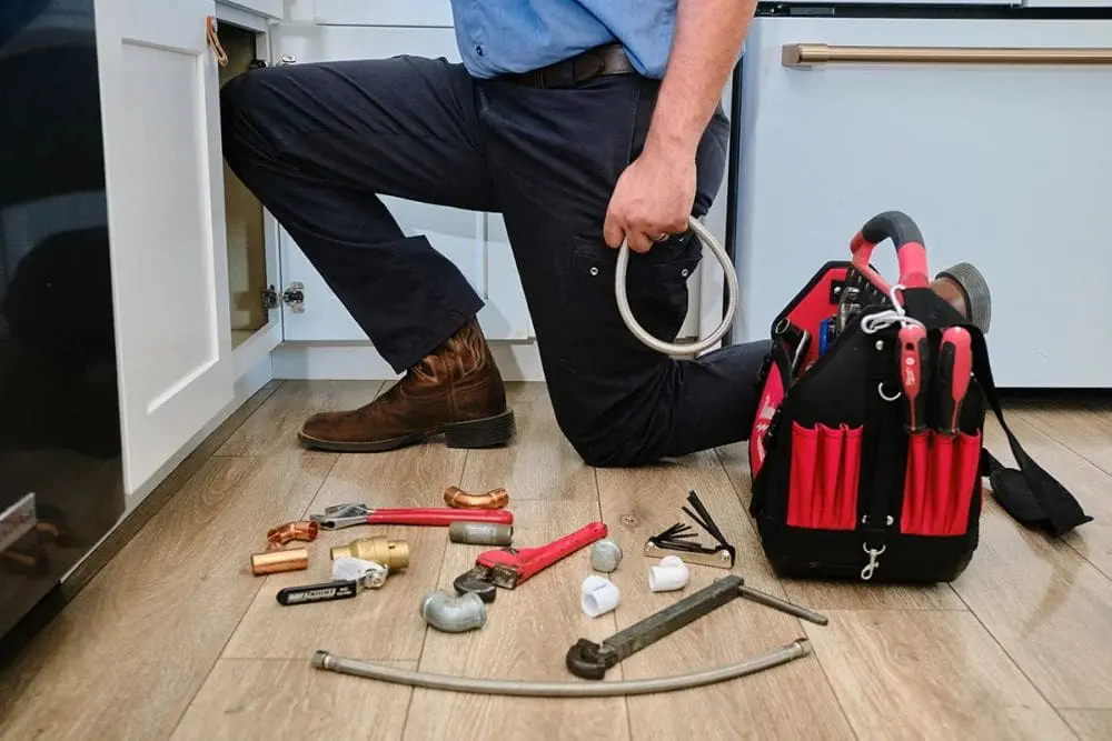Plumbing work area under a sink in Phoenix, Arizona with tools, pipe fittings, and equipment prepared for service. Day & Night Air Conditioning, Heating, and Plumbing provides commercial plumbing in Phoenix AZ, handling pipe repairs, fixture installation, and maintenance for business properties. The setup includes pipe wrenches, fittings, and flexible lines used for plumbing system repairs and inspections. Businesses in Phoenix can contact Day & Night Air Conditioning, Heating, and Plumbing at (602) 584-7758 for commercial plumbing services, including repairs, installations, and maintenance work.