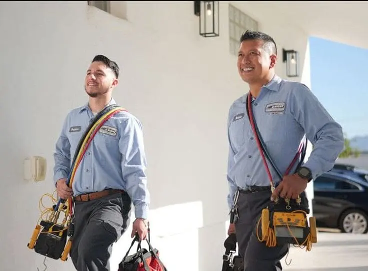 Two Day & Night Air Conditioning, Heating, and Plumbing technicians walking toward a service location in Phoenix, Arizona while carrying plumbing and HVAC tools. The scene represents commercial plumbing in Phoenix AZ, where trained technicians arrive prepared for pipe repair, system installation, and maintenance work. The tools carried include diagnostic equipment, tool bags, and service gear used for plumbing inspections and repairs. Businesses in Phoenix can contact Day & Night Air Conditioning, Heating, and Plumbing at (602) 584-7758 for commercial plumbing services, including repair, installation, and ongoing maintenance support.