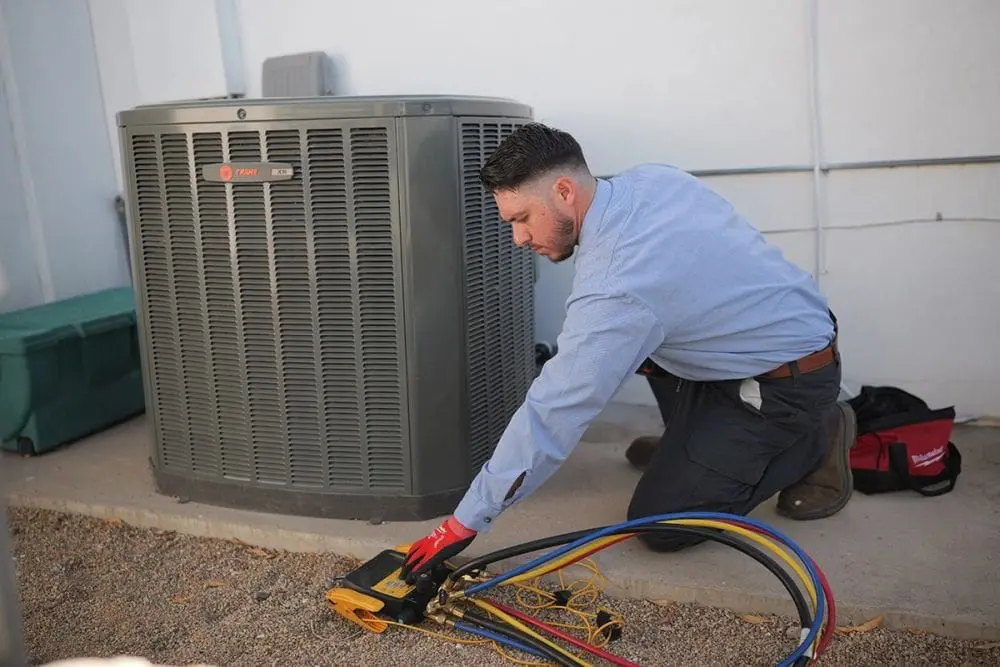 Day & Night Air Conditioning, Heating, and Plumbing technician performing HVAC services in Scottsdale, Arizona while kneeling next to an outdoor AC unit. The technician is using diagnostic gauges connected with hoses to check system pressure and performance. The scene represents HVAC services in Scottsdale including air conditioning repair, system diagnostics, and routine maintenance. Customers can contact Day & Night Air Conditioning, Heating, and Plumbing at (602) 584-7758 for HVAC services in Scottsdale, including repair, installation, and maintenance.