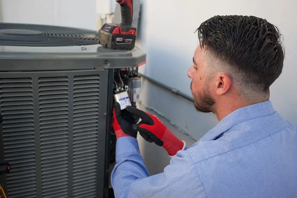 A Day & Night Air Conditioning, Heating and Plumbing technician performs Emergency AC Repair in Peoria, AZ by inspecting and replacing an electrical capacitor inside an outdoor air conditioning unit. The image shows an active cooling system repair with exposed wiring, HVAC components, and service tools used to diagnose the problem. Emergency air conditioner repairs help restore cooling quickly when systems stop working during hot Arizona weather.