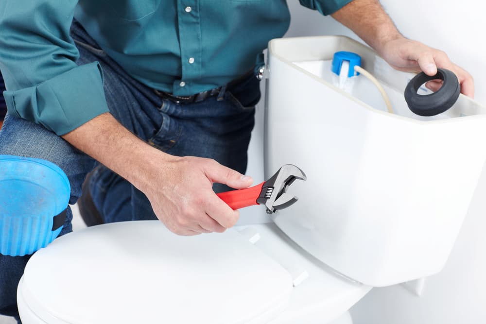 person fixing running toilet with a wrench